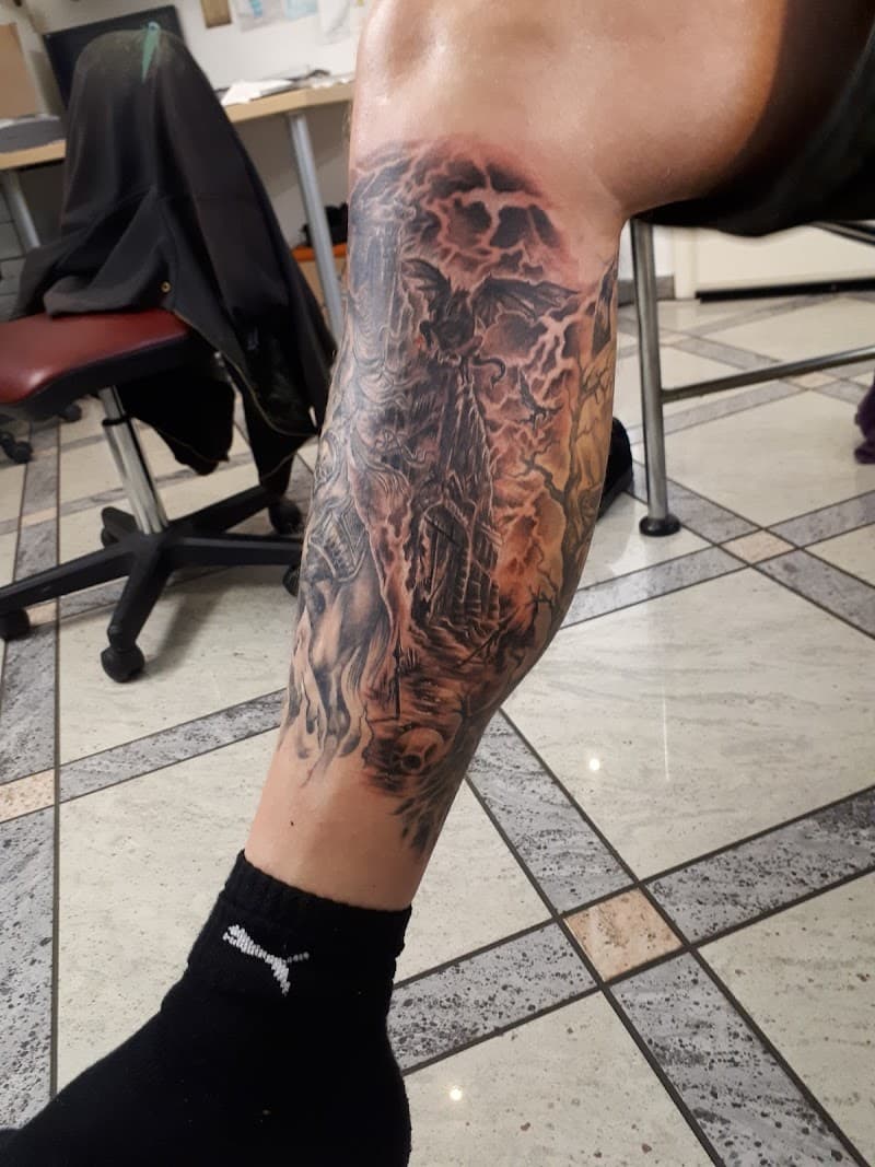 Grote zwart-wit tattoo van een duister kasteel met draak en schedels op kuit.