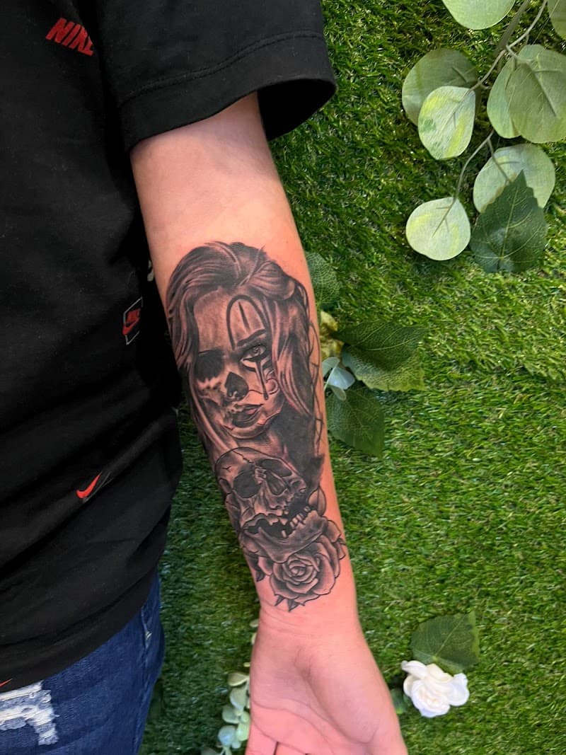 Black and grey tattoo van een vrouw met doodskop make-up, een schedel en een roos.