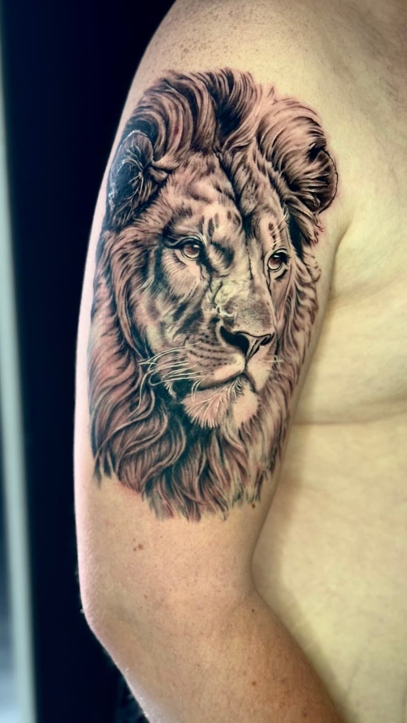 Realistische leeuwenkop tattoo op de bovenarm.