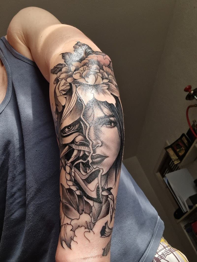 Zwart-wit tattoo van een vrouwengezicht dat overgaat in een Hannya masker met bloemen.