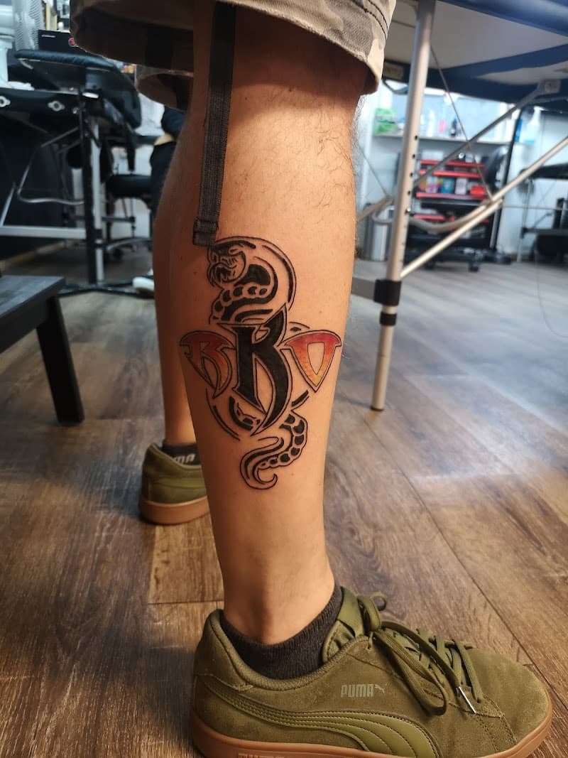 Cobra slang met 'RKO' letters in tribal stijl op onderbeen.