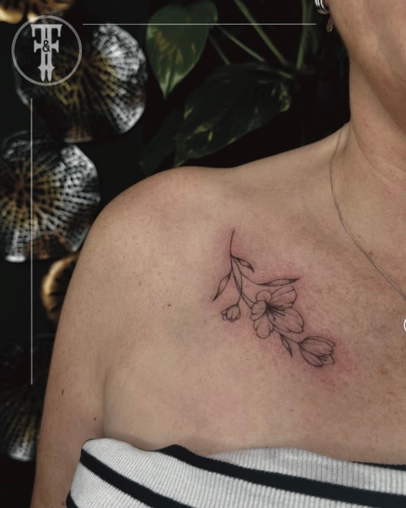 Fineline bloementak tattoo op het sleutelbeen.