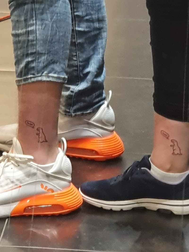 Twee kleine, minimalistische dinosaurus tattoos op enkels.