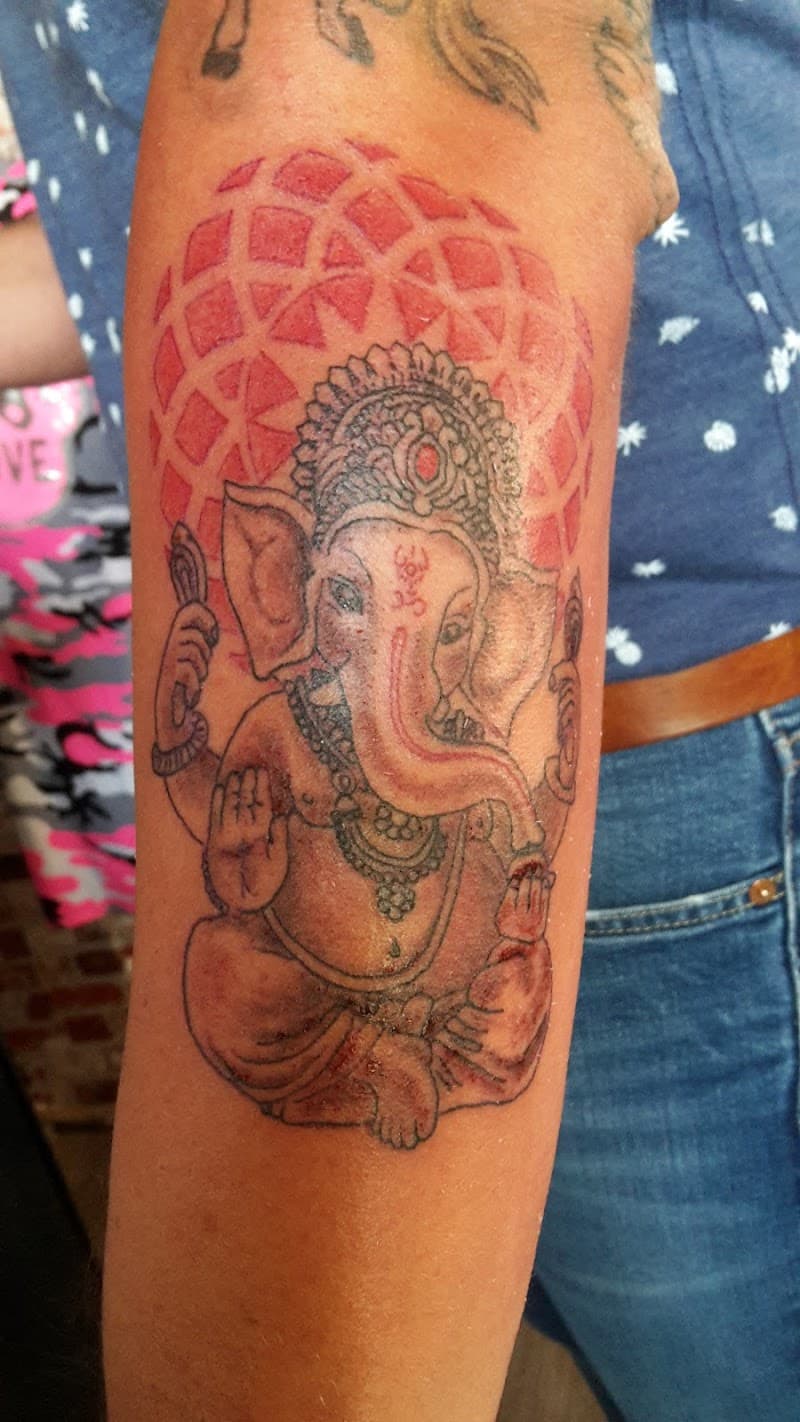 Ganesha tattoo met rode geometrische achtergrond op onderarm.