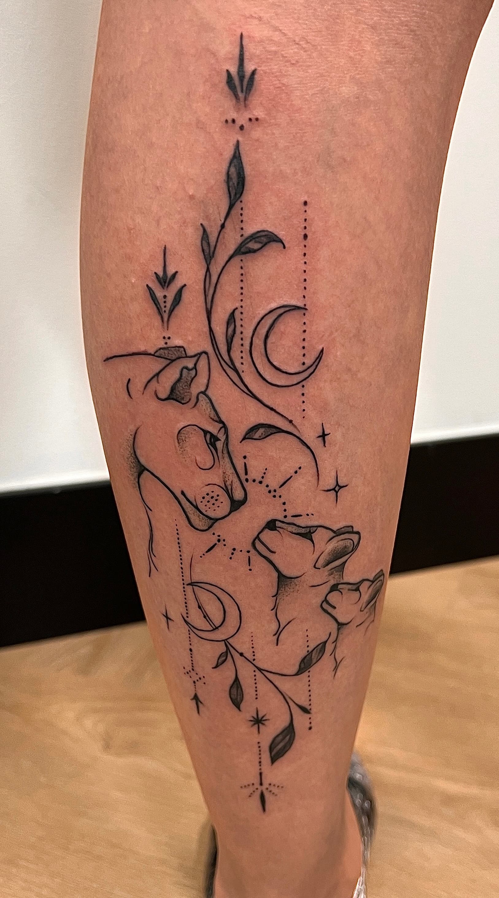 Fineline tattoo van een leeuwin met twee welpjes, maan en sterren.