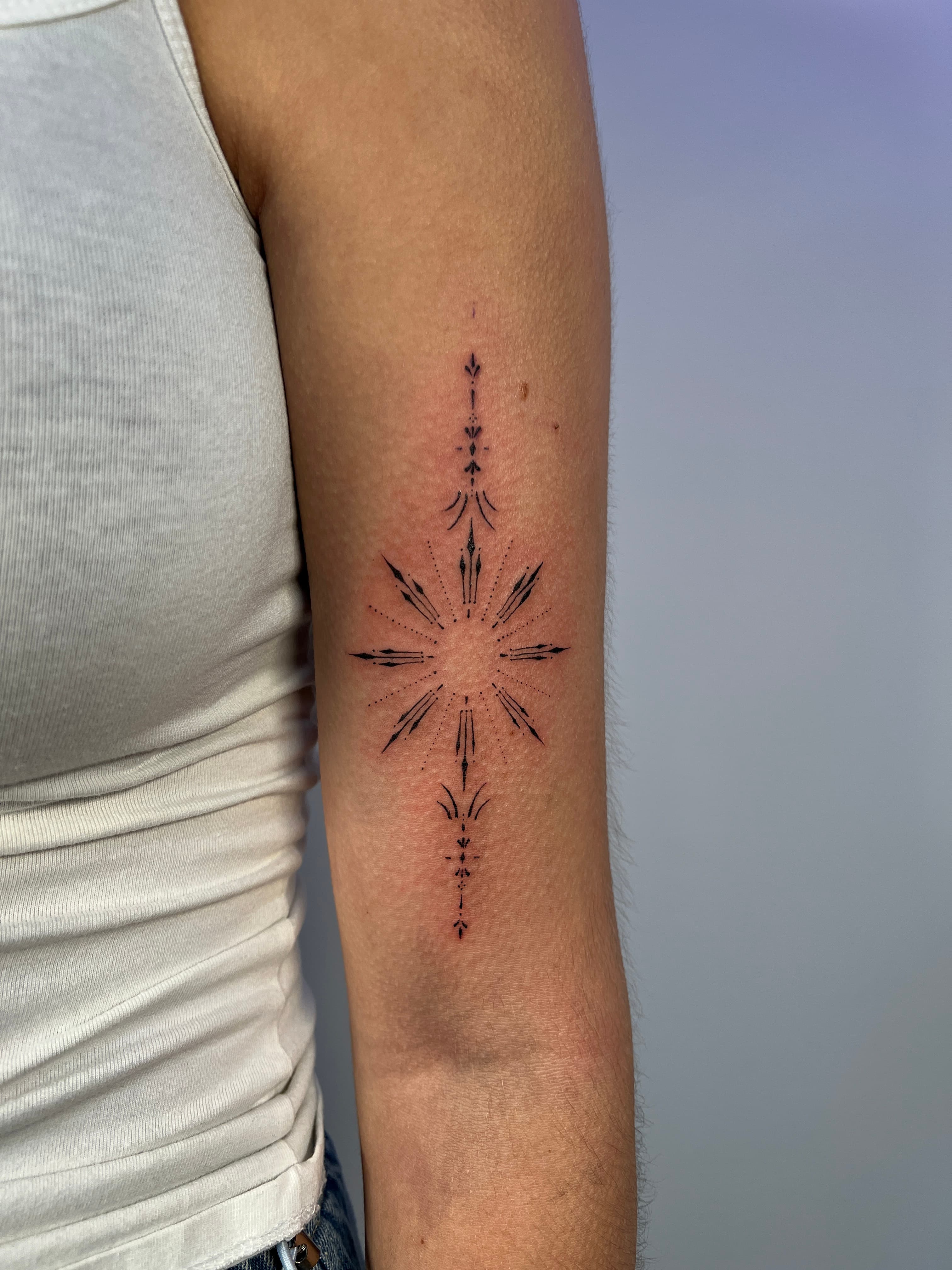Fineline ornamentale ster tattoo op bovenarm met dotwork details.