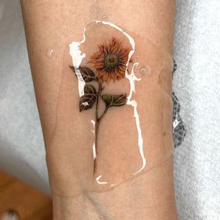 Realistische zonnebloem tattoo in kleur op de onderarm.