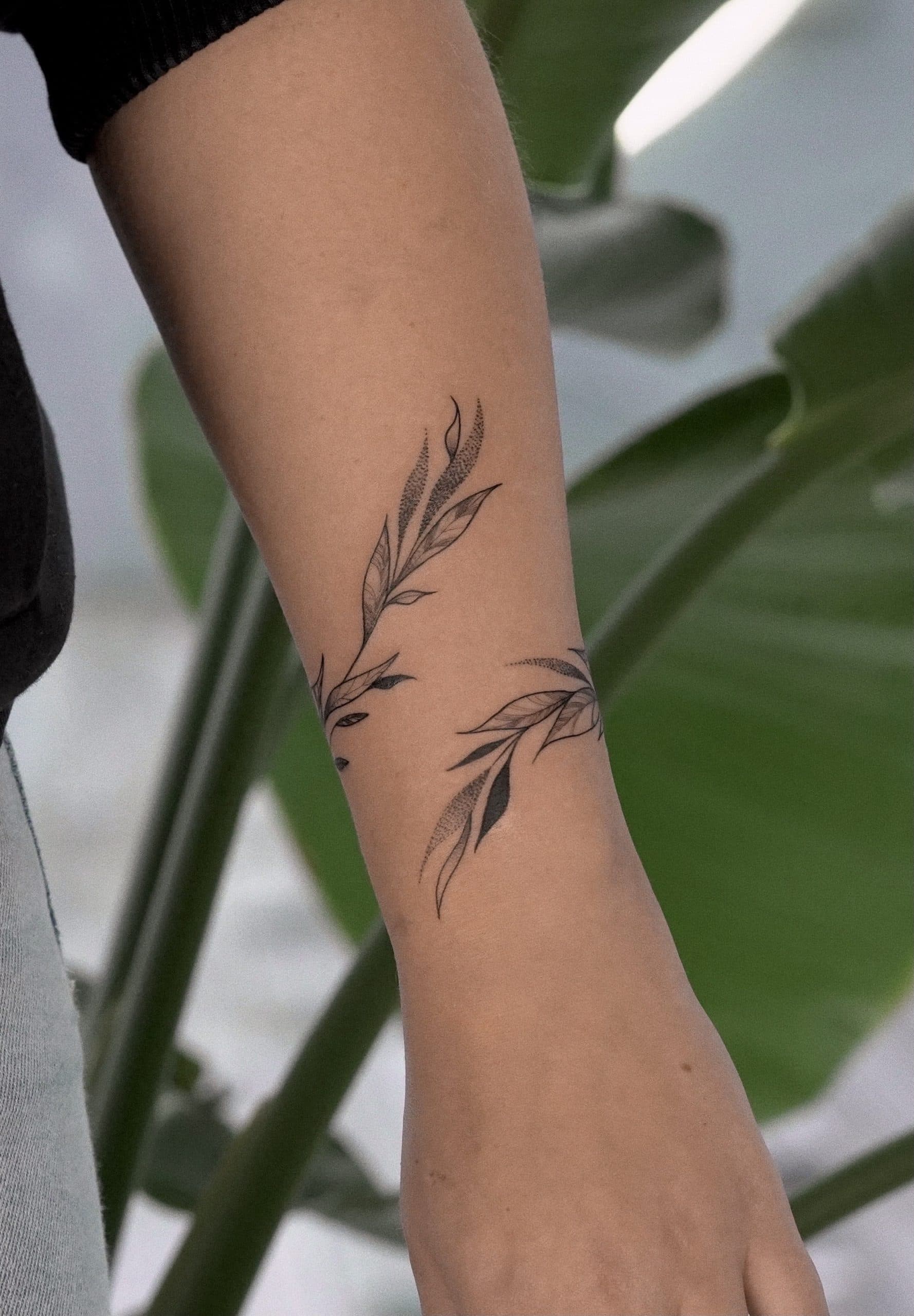 Fineline bladeren en takken tattoo die om de onderarm wikkelt.