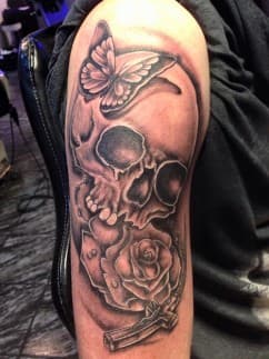 Zwart-wit tattoo van een schedel met een vlinder en een roos met kruis.