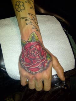 Grote rode roos tattoo op de hand, met groene bladeren.