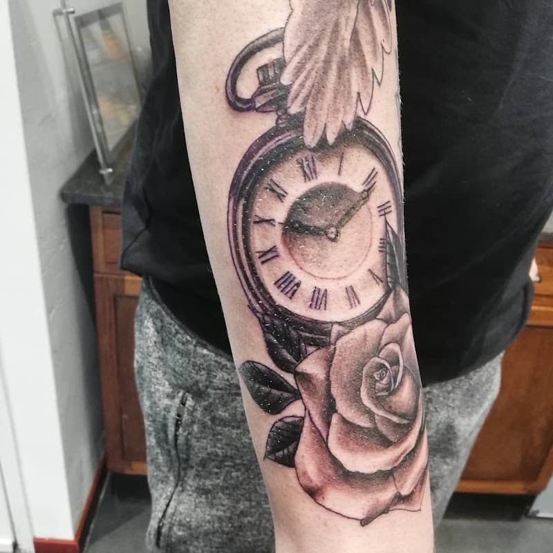 Zwart-wit tattoo van een zakhorloge en een roos op de onderarm.