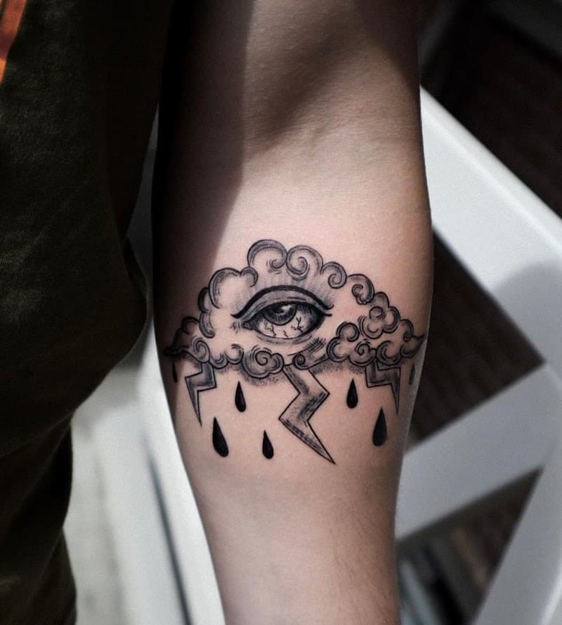 Illustratieve tattoo van een wolk met een oog, bliksem en regen op de bovenarm.