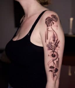 Fineline botanische en geometrische tattoo op bovenarm.