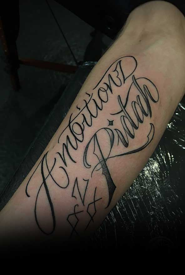 Zwart-wit script tattoo 'Ambitionz Az A Ridah' op onderbeen.