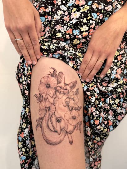 Fineline tattoo van een fennek vos met bloemen op het bovenbeen.