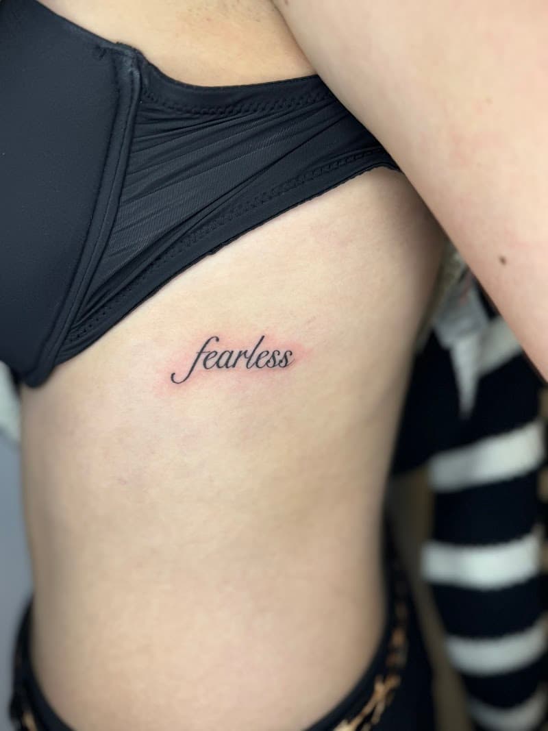 Fineline tattoo van het woord 'fearless' op de ribben.