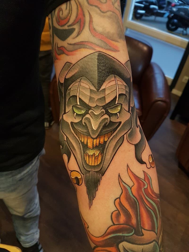 Neo-traditional tattoo van een duistere narrenkop op de bovenarm.