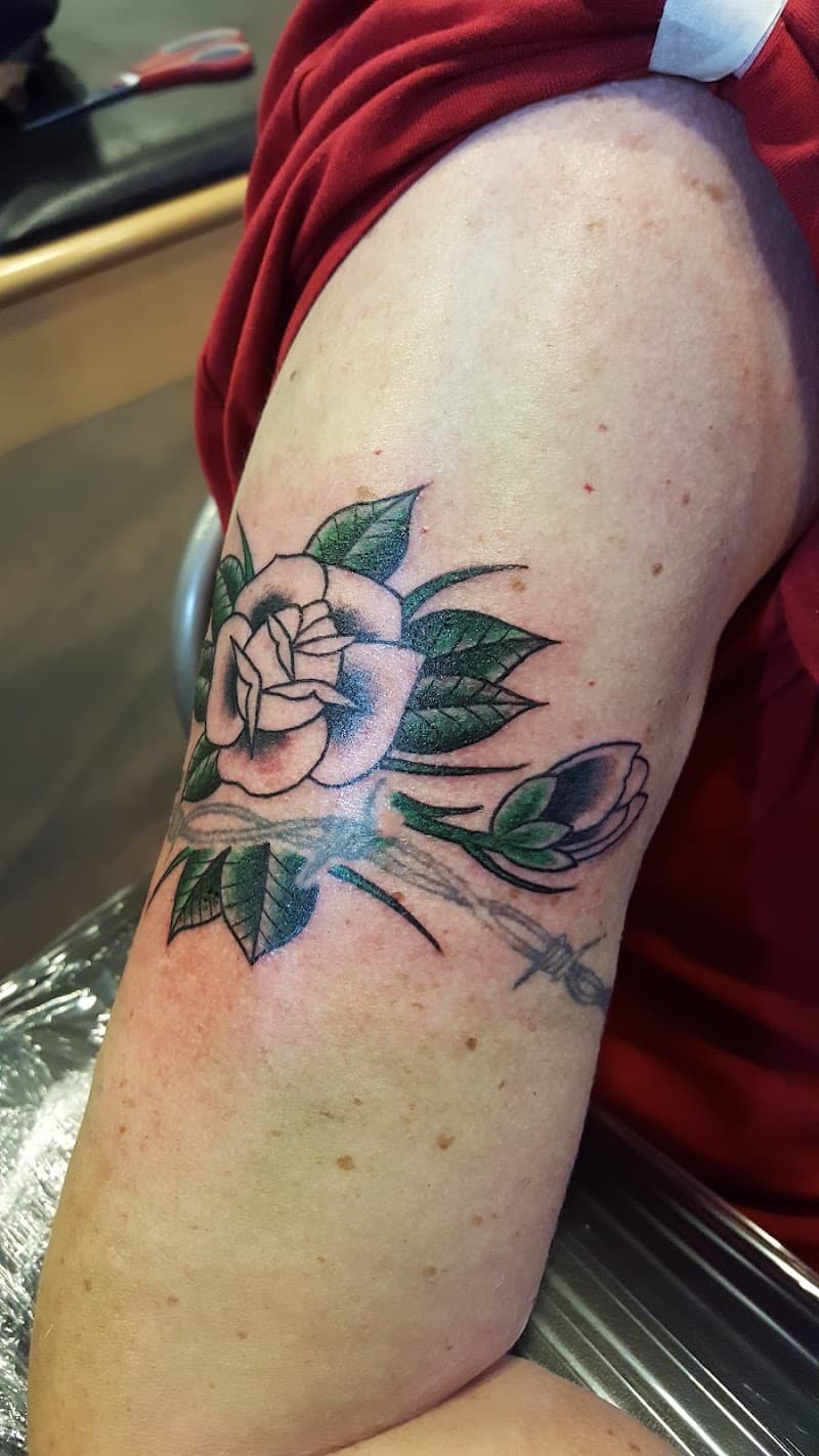 Witte roos met groene bladeren, knop en prikkeldraad op bovenarm.