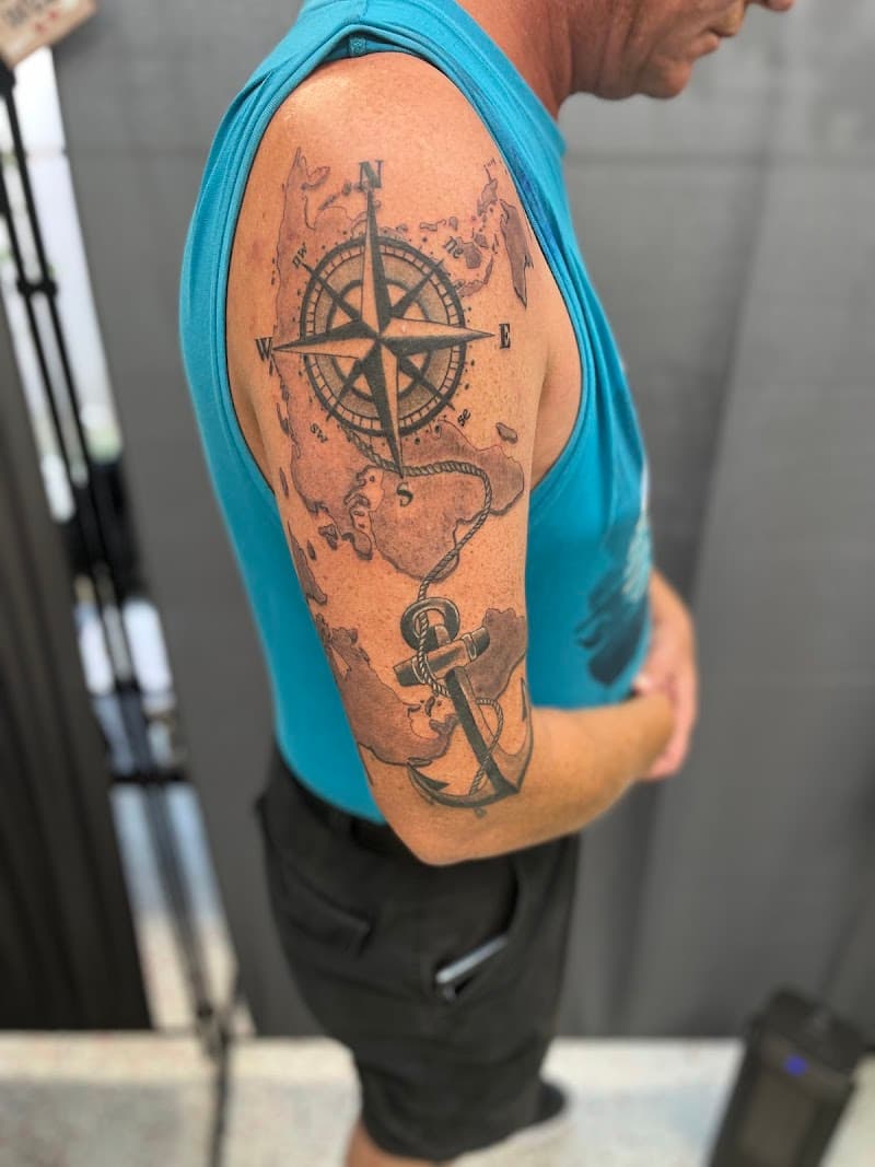 Kompas, anker en wereldkaart tattoo op bovenarm in blackwork stijl.