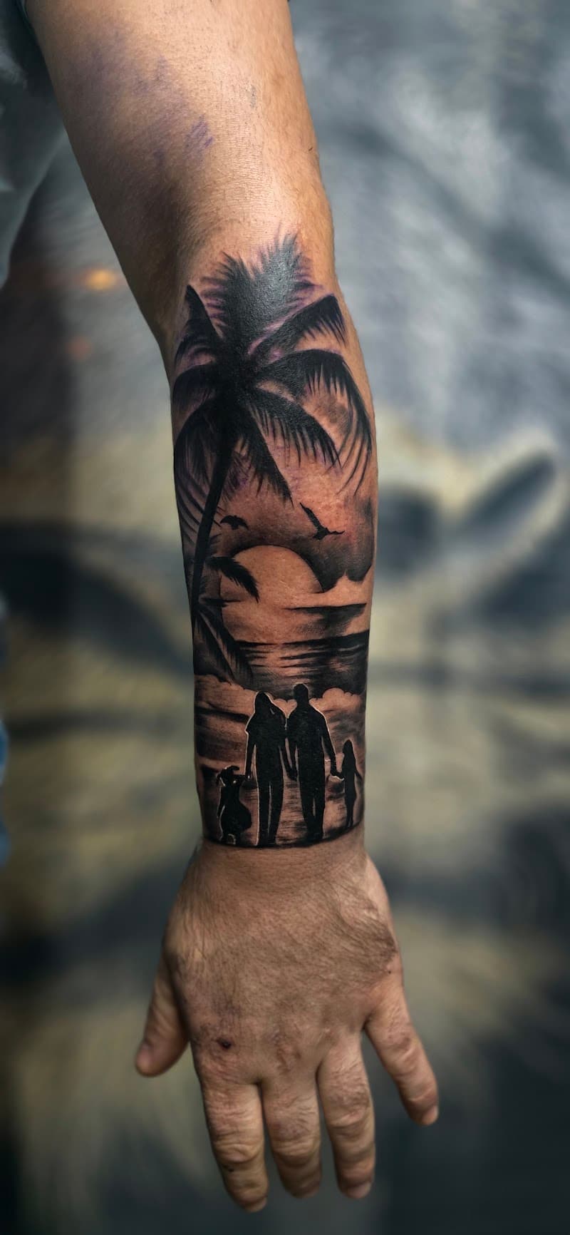 Zwart-wit silhouet tattoo van een gezin op het strand bij zonsondergang.