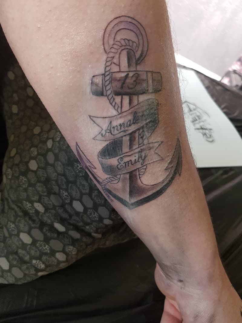 Zwart-wit anker tattoo met namen 'Annale', 'Emily' en nummer '13' op onderarm.
