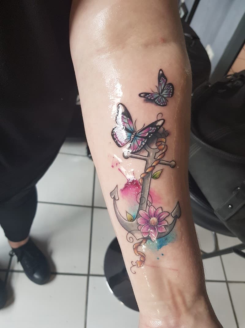 Kleurrijke anker tattoo met vlinders en bloem in watercolor stijl.