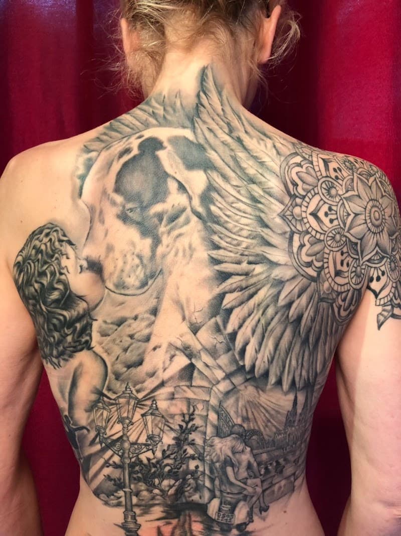 Grote rugtattoo met een engel die een hond kust, een mandala en een straatscène.