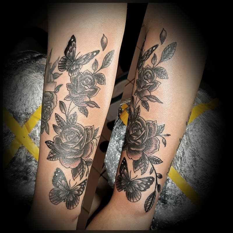 Zwart-wit tattoo van rozen en vlinders op beide onderarmen.