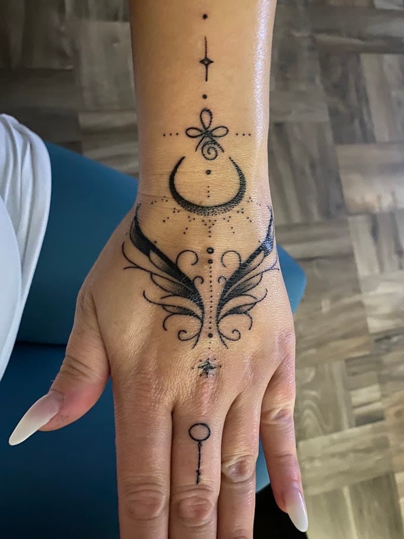 Decoratieve dotwork tattoo op hand en pols met maan, unalome en sleutel.