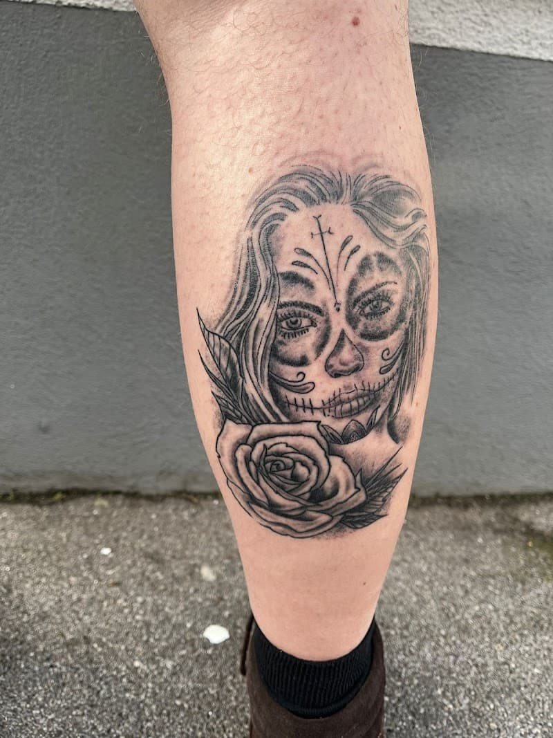 Zwart-wit tattoo van een Day of the Dead vrouw met een roos op het onderbeen.