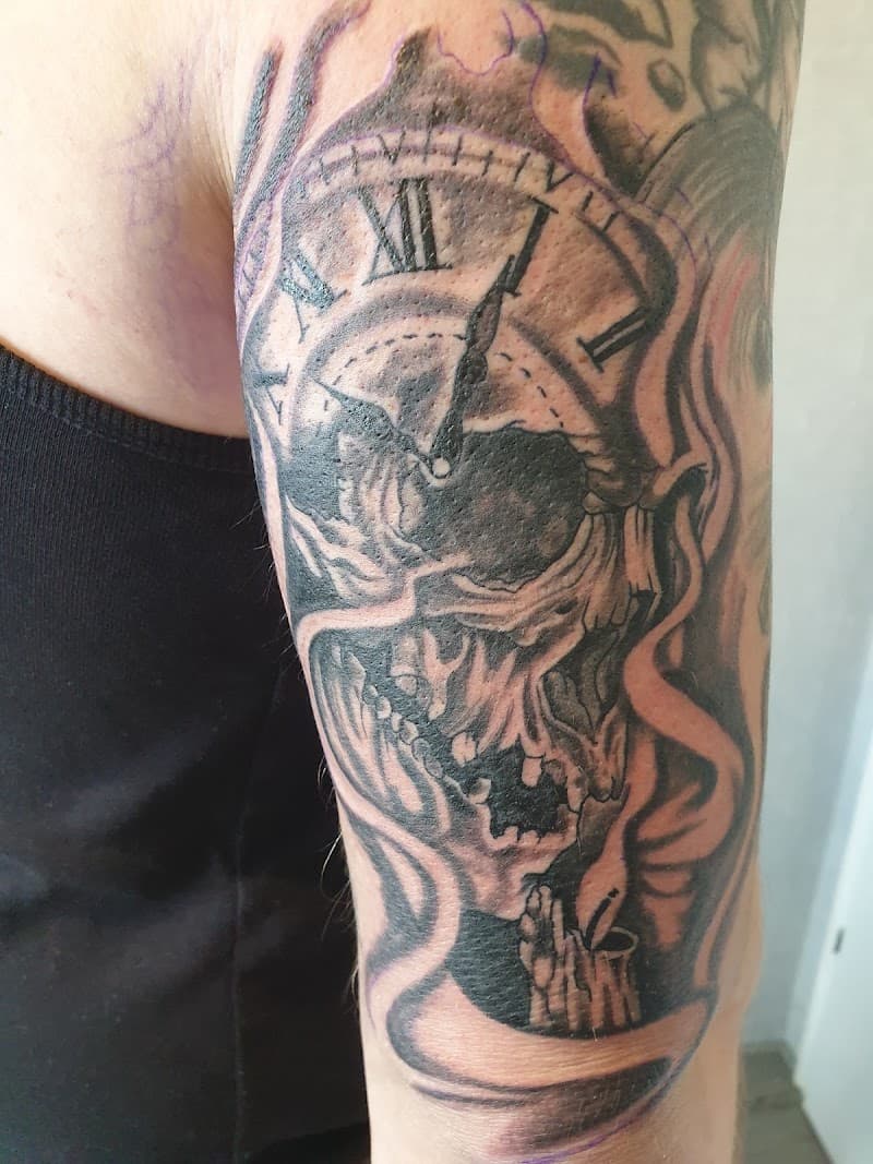Zwart-wit tattoo van een schedel met een klok en een brandende kaars op de bovenarm.
