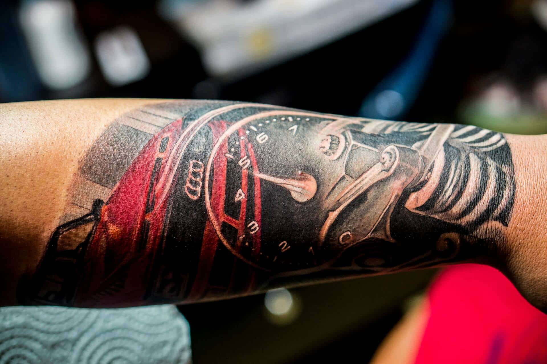 Realistische tattoo van een rode Audi en een toerenteller op een onderarm.