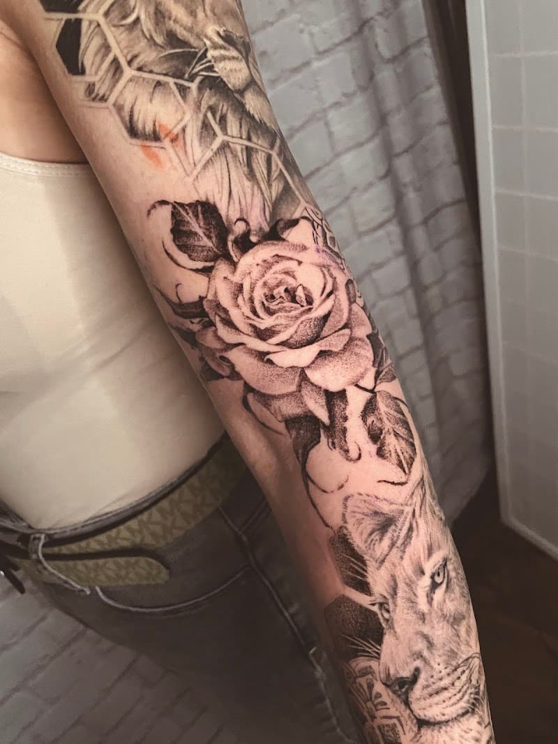 Zwart-wit tattoo van een roos, leeuwenkop en geometrische vormen op de arm.