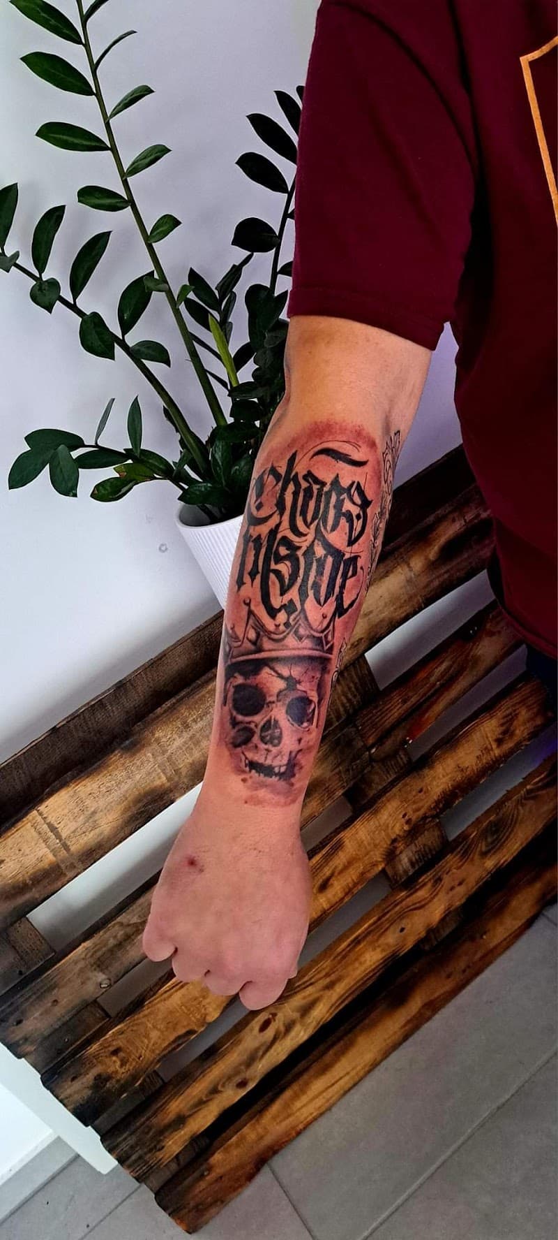 Schedel met kroon en 'Chaos Inside' tekst op onderarm.