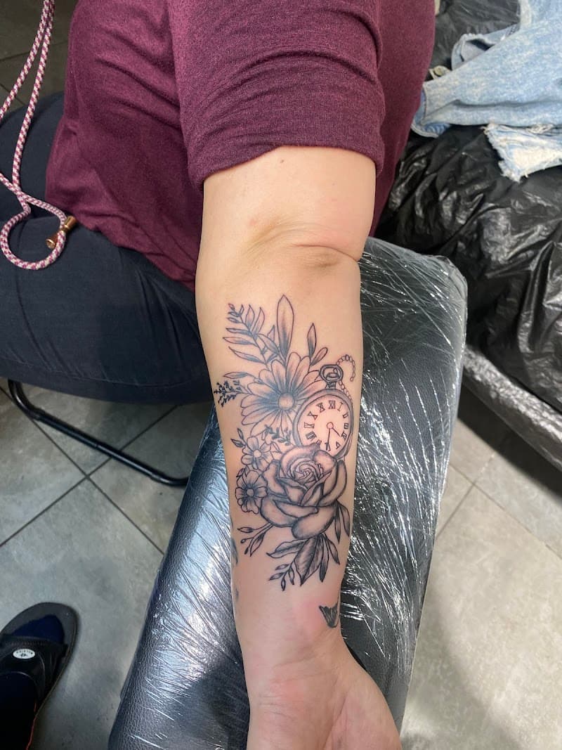 Fineline tattoo van een zakhorloge met bloemen en bladeren op de onderarm.