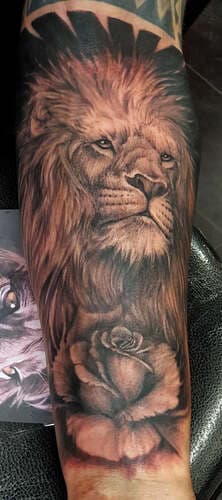 Realistische leeuwenkop met roos op onderarm.