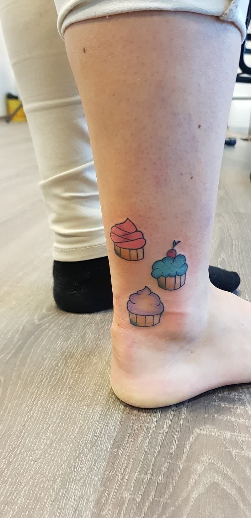 Drie kleine, kleurrijke cupcake tattoos op de enkel.