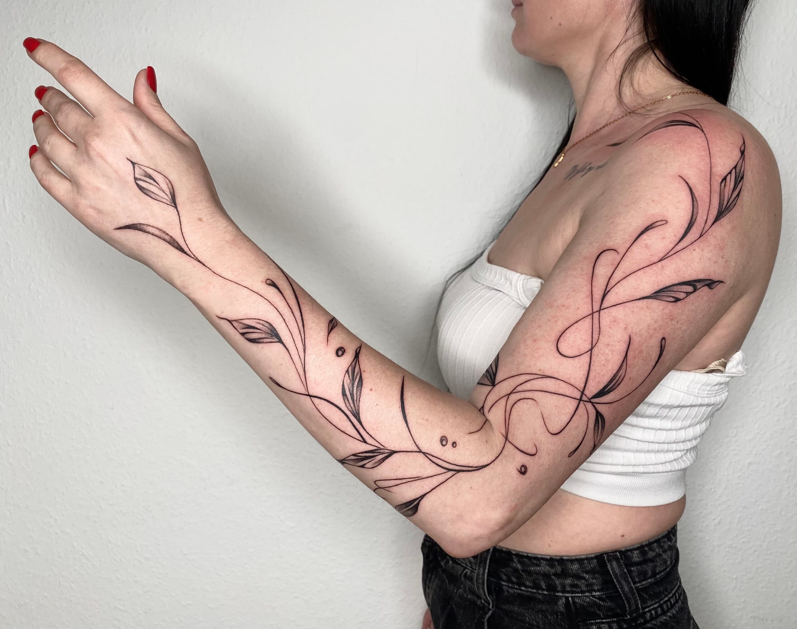 Elegante fineline tattoo van sierlijke bladeren en lijnen over de hele arm.