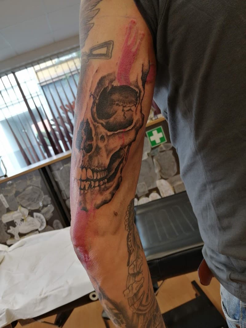 Grote schedel tattoo in blackwork stijl op de bovenarm en elleboog.