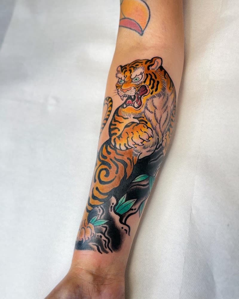 Japanse stijl tijger tattoo op onderarm, met golven en bladeren.