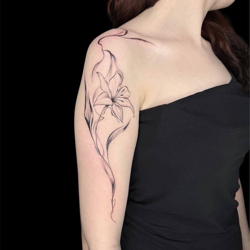 Fineline lelie met vloeiende lijnen op bovenarm en schouder.
