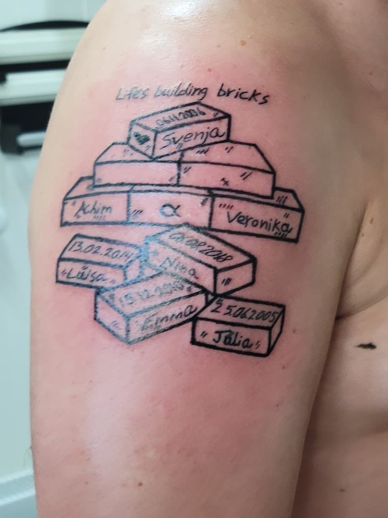 Illustratieve tattoo van bakstenen met namen en datums op bovenarm.