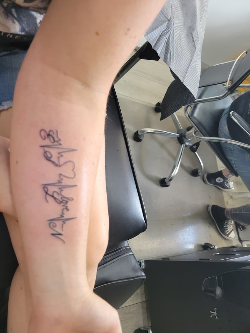 Fineline hartslag tattoo met woord op onderarm.