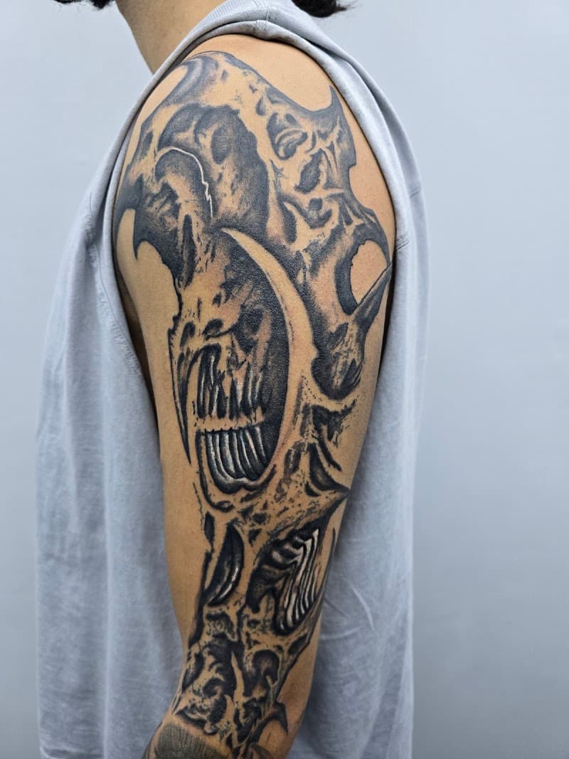 Gedetailleerde biomechanische schedel tattoo op de bovenarm in zwart-wit.