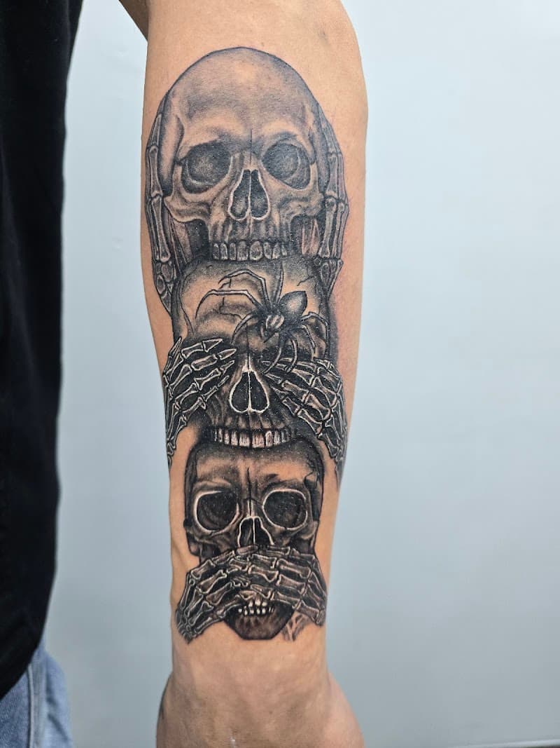 Zwart-wit tattoo van drie schedels die 'horen, zien en zwijgen' uitbeelden.