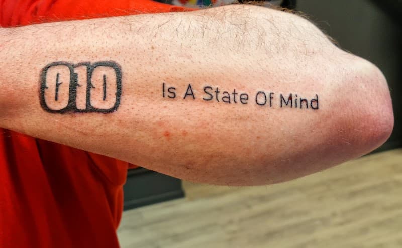 Tattoo met '010' in een kader en de tekst 'Is A State Of Mind' op de bovenarm.