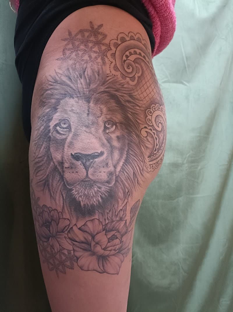 Realistische leeuwenkop met bloemen en ornamenten op bovenbeen.