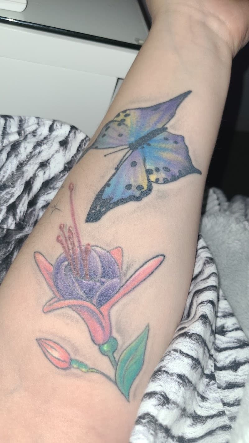 Kleurrijke vlinder en fuchsia bloem op onderarm.