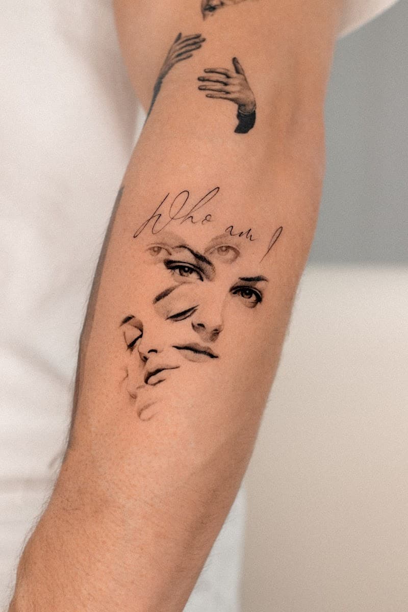Fineline tattoo van overlappende gezichten en tekst 'Who am I' op de bovenarm.