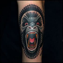Traditionele gorilla kop tattoo met open bek op onderarm.